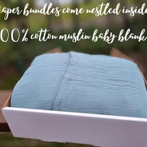 May include: A folded, light blue 100% cotton muslin baby blanket rests inside a white box with a brown interior. The text on the image reads: "diaper bundles come nestled inside a 100% cotton muslin baby blanket."