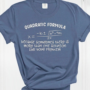 May include: A blue t-shirt with the text "QUADRATIC FORMULA" and a mathematical equation printed in white. The text below the equation reads "because sometimes there is more than one solution for your problem."