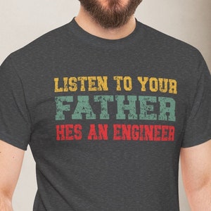 Könnte beinhalten: Ein dunkelgraues T-Shirt mit dem Text "Listen to your Father He's an Engineer" in einer Vintage-Schriftart mit gelben, grünen und roten Farben.
