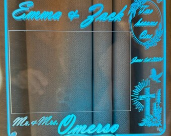 May include: A blue acrylic picture frame with a white background and a white border. The frame has the text "Emma & Jack" and "Two Became One" on the top. The bottom of the frame has the text "Mr. & Mrs. Omerso". The frame is lit up with a blue light and has a remote control with multiple colored lights.