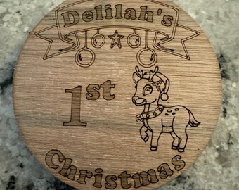 May include: A wooden Christmas ornament with the text "Delilah's 1st Christmas" and a cartoon reindeer with a bell around its neck.
