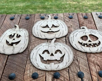 May include: Four wooden pumpkin cutouts with different carved jack-o'-lantern faces. The pumpkins are arranged on a rustic wooden surface.