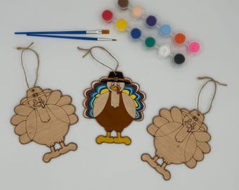 May include: Three unfinished wooden turkey ornaments with paint and brushes for a Thanksgiving craft project.