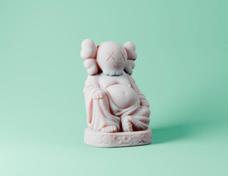 May include: A white ceramic figurine of a Buddha with a stylized face and crossed eyes. The figurine is sitting in a meditative pose with its hands resting in its lap.