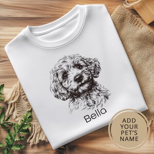 May include: White t-shirt with a black and white line drawing of a dog's head. The dog's name, "Bella", is printed below the image. The text "ADD YOUR PET'S NAME" is printed on a circle in the lower right corner.