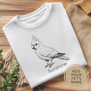 May include: White t-shirt featuring a black and white illustration of a cockatoo and the text "Sunshine".