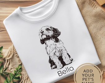 May include: White t-shirt with a black and white illustration of a dog sitting. The text "Bella" is printed below the dog. The text "ADD YOUR PET'S NAME" is printed in a circle on the bottom right corner of the shirt.