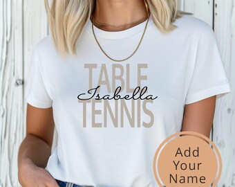 May include: White t-shirt with the text "TABLE TENNIS" in brown letters and the name "Isabella" in black cursive writing.