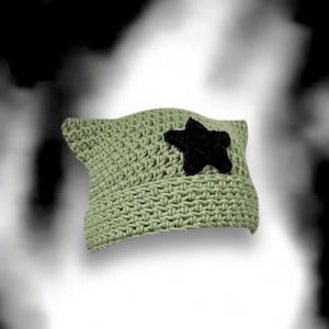 Pode incluir: Um chapéu de crochê verde com uma estrela preta na frente.