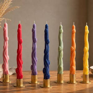 May include: Seven tall taper candles in pink, red, purple, dark blue, light green, orange, and yellow. Each candle features a raised, swirling floral vine design and is held upright by a simple, cylindrical, brushed gold metal candle holder.