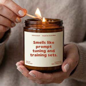 May include: A brown glass jar candle with a cream label featuring the text: DASHO SHOP, MADE IN CALIFORNIA, Smells like prompt tuning and training sets., SCENT OF COFFEE SHOP, COCONUT SOY WAX CANDLE 7.5 OZ. The candle has a lit wick.