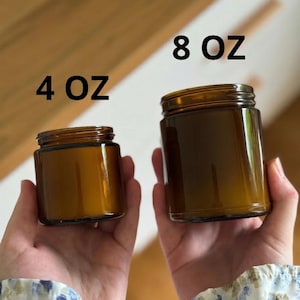 Two hands holding brown glass jars of different sizes, with the larger jar labeled as 4 oz and the smaller one labeled as 8 oz.