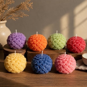 May include: A collection of seven spherical candles, each featuring a textured, overlapping petal design. The candles are presented in a variety of colors including purple, orange, light green, red, yellow, blue, and pink, each with a central wick.
