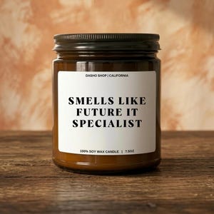 May include: A brown glass jar candle with a black lid. The label reads "SMELLS LIKE FUTURE IT SPECIALIST." The candle is 213g and made of 100% soy wax. The jar is on a wooden surface.