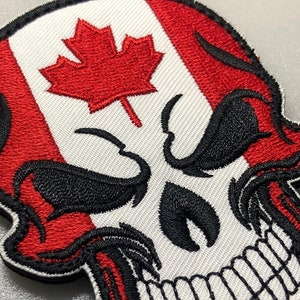 May include: A white skull with a red and white Canadian flag design. The skull has black eyes and a wide, toothy grin.