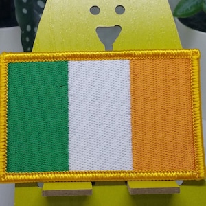 May include: A green, white, and orange embroidered patch with a gold border, depicting the flag of Ireland.
