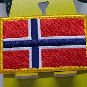 May include: An embroidered patch featuring the Norwegian flag, with red, white and blue colours and a gold border.
