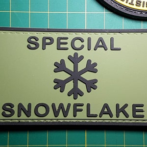 May include: A green and black patch with the text "SPECIAL SNOWFLAKE" and a black snowflake graphic.