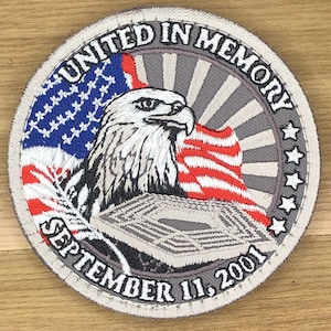 May include: Circular patch with the text "UNITED IN MEMORY" and "SEPTEMBER 11, 2001". The patch features an American flag, an eagle, and an image of the Pentagon. The border is gray with white stars.