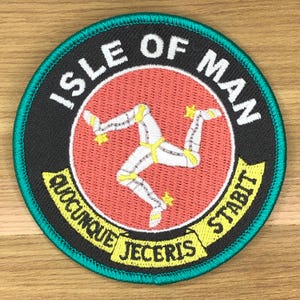 Könnte beinhalten: Runder, gestickter Aufnäher mit dem Triskelion der Isle of Man, einem dreibeinigen Symbol, auf rotem Hintergrund. Der Aufnäher enthält den Text "ISLE OF MAN" und das Motto "QUOCUNQUE JECERIS STABIT" in Weiß und Gelb.