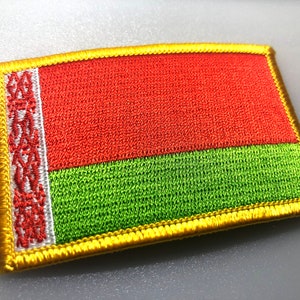 May include: A red and green embroidered patch with a white and red design in the corner. The patch is surrounded by a gold border.