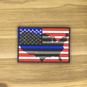 Op de afbeelding: Geborduurde patch met het ontwerp van de vlag van de Verenigde Staten met een blauwe lijn en de omtrek van de Amerikaanse kaart. De patch heeft een rood-wit gestreepte achtergrond met een blauw vierkant in de linkerbovenhoek met witte sterren.