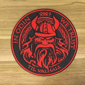 May include: Circular black patch with a red Viking design. The patch shows a red Viking figure with a horned helmet and a long beard. The text "IN ODIN WE TRUST TIL VALHALL" is embroidered around the image.