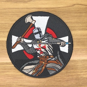 May include: Embroidered patch featuring a medieval knight in armor, wielding an axe and a spear. The knight is positioned in front of a white cross with a red outline, set against a black circular background. The patch is approximately 3.5 inches in diameter.