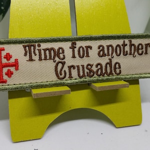 Pu&ograve; includere: Una toppa ricamata verde e beige con una croce rossa e il testo "Time for another Crusade".