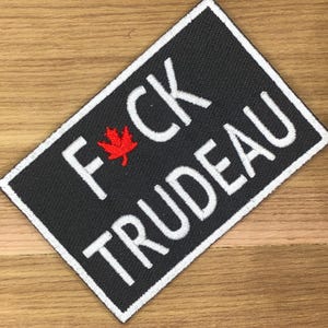 May include: A rectangular black patch with white embroidered text that reads "F*CK TRUDEAU". A red maple leaf is between the F and the C. The patch has a white border.