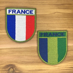 May include: Two embroidered patches with the word "FRANCE" at the top. One patch features the French flag colors: blue, white, and red. The other patch has blue, green, and light green vertical stripes.