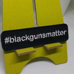 May include: Black embroidered patch with white text that reads "#blackgunsmatter" on a yellow background.