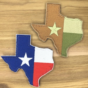 Op de afbeelding: Twee geborduurde patches in de vorm van de staat Texas. Eén patch heeft het ontwerp van de Texas-vlag in blauw, wit en rood. De andere patch heeft een bruin, groen en beige kleurenschema met een ster in het midden.