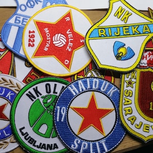 Peut inclure: Une collection de patchs brodés représentant différents logos d'équipes sportives. Les patchs sont circulaires et rectangulaires, avec une variété de couleurs et de motifs. Certains des logos incluent les noms des équipes, tels que "Borac", "Hajduk", "Velez" et "Rijeka".