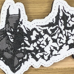 May include: Embroidered patch featuring Batman's silhouette in shades of gray and black. The patch has a white border with a scalloped edge and a design of bats. Ideal for jackets, bags, or other fabric items.