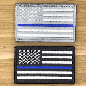 Könnte beinhalten: Zwei gestickte Aufnäher mit dem Design der amerikanischen Flagge und einer blauen Linie. Ein Aufnäher ist silber und grau, der andere schwarz und weiß. Beide haben einen blauen Streifen, der die Unterstützung der Strafverfolgung darstellt.