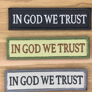 May include: Three rectangular embroidered patches with the phrase "IN GOD WE TRUST". The top patch is black with white text, the middle patch is olive green with brown text, and the bottom patch is gray with white text.