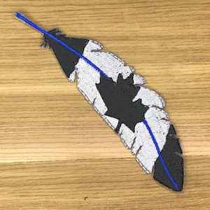 May include: Embroidered feather patch featuring a black and white design with a blue accent. The feather has a detailed, textured appearance, with a central blue line. The patch is likely for decorative purposes, suitable for clothing or accessories.