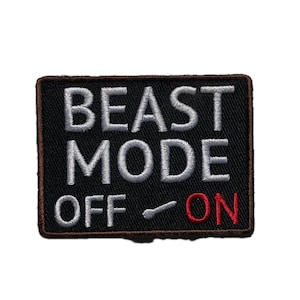 Peut inclure: Un écusson noir brodé avec les mots "BEAST MODE OFF ON" en blanc et rouge. L'écusson a une bordure marron et un graphique de commutateur.