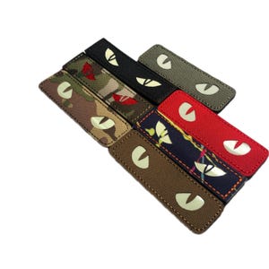May include: A selection of rectangular patches with an eye design. The patches feature various patterns, including camouflage, floral, and solid colours like black and red. The eye design is a glowing, off-white colour.