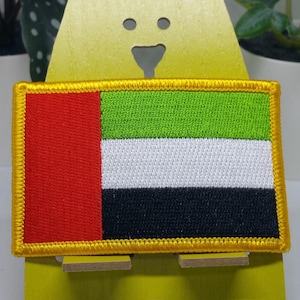 Op de afbeelding: Een geborduurde patch in rood, wit, zwart en groen met een gouden rand, die de vlag van de Verenigde Arabische Emiraten voorstelt.