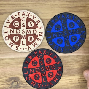 May include: Three round embroidered patches with the text "LIV B PAX VR" and other symbols. The patches are in cream, navy blue, and black, with the text in brown, blue, and red. The patches have a cross design.