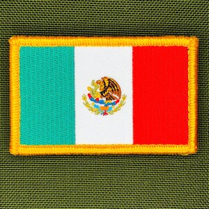 May include: Embroidered patch featuring the Mexican flag. The flag design includes vertical stripes of green, white, and red, with the Mexican coat of arms in the center. The patch has a gold border and is set against a green textured background.