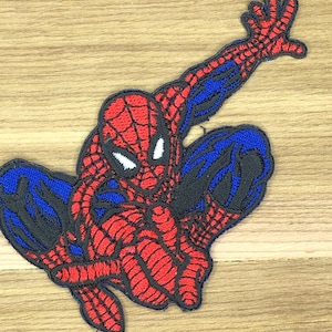 May include: Embroidered patch of Spider-Man in a dynamic pose. The patch features the superhero's iconic red and blue suit with black webbing details. The design is detailed and vibrant, suitable for adding to clothing or accessories.
