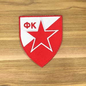 May include: An embroidered patch in red and white, featuring a shield shape with a central red star. The patch includes the white letters "ФК" on a white background.