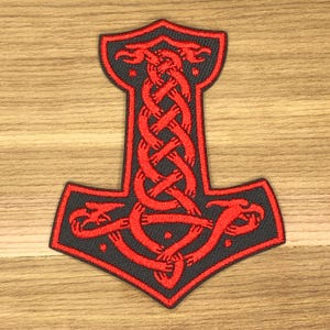 Könnte beinhalten: Gestickter Aufnäher mit dem roten und schwarzen Design von Thors Hammer, Mjölnir. Der Aufnäher hat ein detailliertes, verschlungenes Muster in Rot auf schwarzem Hintergrund. Die Hammerform ist schwarz umrandet.