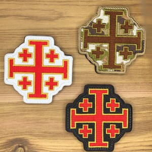 Könnte beinhalten: Drei Jerusalemkreuz-Patches. Einer ist rot und weiß mit goldenem Rand. Ein weiterer ist Camouflage mit einem braunen Kreuz. Der dritte ist schwarz mit einem roten Kreuz und goldenem Rand. Alle haben ein Kreuzdesign.