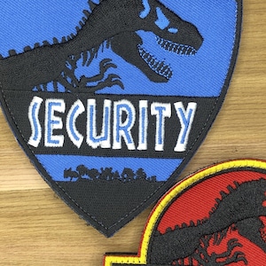 May include: Embroidered patch featuring a black dinosaur silhouette on a blue background. The word "SECURITY" is embroidered in white block letters. The patch has a black border.
