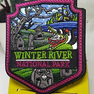 May include: Embroidered patch with a dark green, black, and white design of a spooky landscape with a castle, trees, and a monster with a toothy grin. The text "WINTER RIVER NATIONAL PARK" is in white on a black background.
