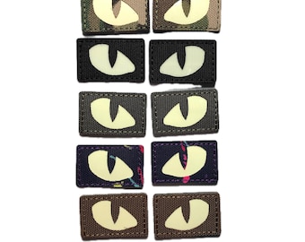 May include: A collection of rectangular patches featuring glowing eye designs. The patches have various background patterns, including camouflage, black, and patterned fabrics. The eyes glow with a bright, off-white color.